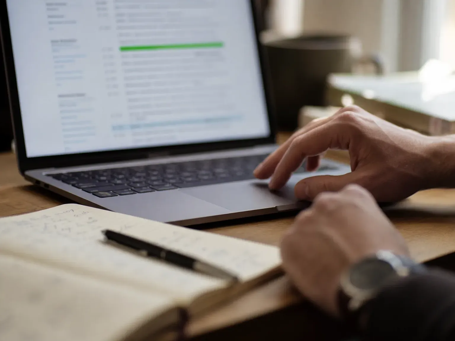 A close, human detail: a researcher's hands resting near a laptop with a transcript on screen and a notebook alongside.